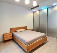 Hálószoba fa ággyal, éjjeliszekrényekkel és fa dekorációjú padlóval egy háromszobás lakásban.