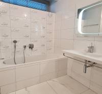 Fürdőszoba káddal és csempékkel egy háromszobás lakásban, fehér és szürke színárnyalatokban.