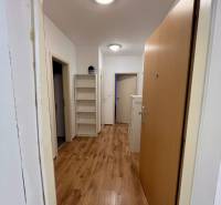 Folyosó egy kétszobás lakásban, fa mintázatú padlóval és polcokkal a falon.