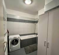 Fürdőszoba mosógéppel, káddal és fehér csempével egy kétszobás lakásban.