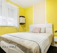 Hálószoba családi házban sárga falakkal, fehér ággyal és virágos dekorációval.