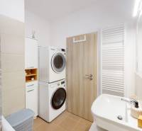 Fürdőszoba egy háromszobás lakásban mosógéppel, szárítógéppel és zuhanyfüggönnyel.