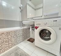 Fürdőszoba káddal és mosógéppel egy kétszobás lakásban, csempe és fehér burkolatok.