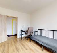 Szoba egy háromszobás lakásban fa mintázatú padlóval, íróasztallal és ággyal.