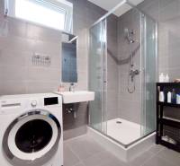 Fürdőszoba egy háromszobás lakásban mosógéppel, zuhanyzóval és mosdóval.