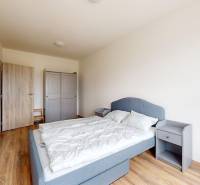 Hálószoba egy háromszobás lakásban, fa dekoros padlóval, szürke ággyal és gardróbbal.