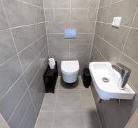 Fürdőszoba fali WC-vel, mosdóval és szürke csempékkel egy háromszobás lakásban.