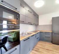 Konyha egy háromszobás lakásban, fa dekor padlóval, szürke szekrények, beépített készülékek.