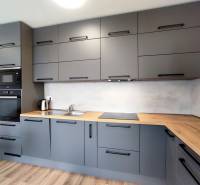 Stílusos konyha egy háromszobás lakásban, fa hatású padlóval és szürke szekrényekkel.