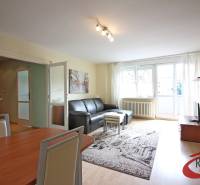 Nappali egy háromszobás lakásban fa mintázatú padlóval és fekete kanapéval.