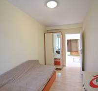 Szoba egy háromszobás lakásban kanapéval, beépített szekrénnyel és fa dekor padlóval.