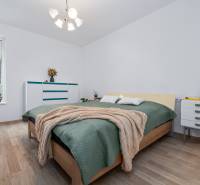 Hálószoba ággyal, komóddal, növényekkel és fa dekorációjú padlóval egy háromszobás lakásban.