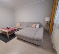 Nappali egy háromszobás lakásban kanapéval és fa dekorációjú padlóval.