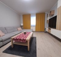 Nappali egy háromszobás lakásban kanapéval, dohányzóasztallal és fa dekorációjú padlóval.