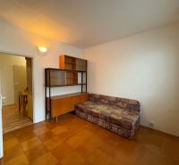 Szoba egy háromszobás lakásban kanapéval, szekrénnyel és fa mintázatú padlóval.