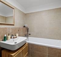 Fürdőszoba mosdóval, tükörrel és káddal egy kétszobás lakásban, világos csempékkel.