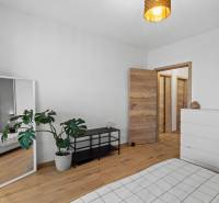 Szoba egy kétszobás lakásban fehér bútorokkal, tükörrel és fa dekorációjú padlóval.