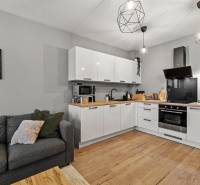 Konyha egy kétszobás lakásban fehér konyhabútorral, szürke kanapéval és fa mintázatú padlóval.