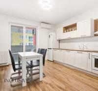 Konyha egy kétszobás lakásban fehér szekrényekkel és fa mintázatú padlóval.