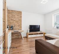 Nappali fa hatású padlóval, TV-vel és krémszínű kanapéval egy kétszobás lakásban.