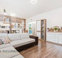 Nappali kétszobás lakásban bézs kanapéval és fa mintázatú padlóval.