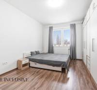 Hálószoba egy kétszobás lakásban, fa mintázatú padlóval, fehér szekrényekkel és szürke részletekkel.