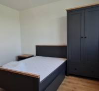 A kétszobás lakás hálószobája tartalmaz egy ágyat, éjjeliszekrényt, ruhásszekrényt és fa dekorációjú padlót.