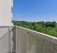 Erkély kilátással az erdőre és dombokra, háttérben egy épület, tiszta égbolt.