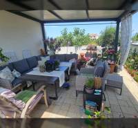 Pihenés a teraszon a nyaraló apartmanban kényelmes ülőalkalmatossággal, virágdíszítéssel és asztallal.