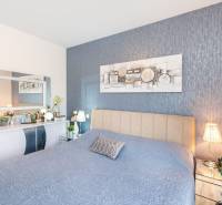 Hálószoba a nyaraló apartmanban kék ágytakaróval, dekorációkkal és tükörrel az asztal felett.