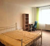 Hálószoba ággyal, asztallal, polccal és fa dekoros padlóval egy kétszobás lakásban.