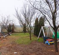 Vizsolyi családi ház kertje fákkal és gyerekhintával a gyepen.