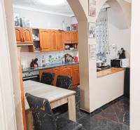 Családi ház konyhája íves bejárattal, fa szekrényekkel és fekete padlóval.