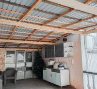 Családi ház: Fém tetős kocsibeálló, rattan székek, műnövények, tárolóhelyek.