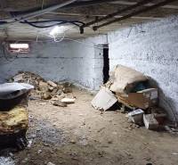 Családi ház alagsora földpadlóval, néhány dobozzal és fával.