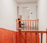 Lépcsőház fa korláttal családi házban, fehér falak, világítás izzóval.