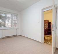 Szoba egy 4 szobás lakásban, fehér falak, szőnyegpadló, nagy ablak és ajtó.