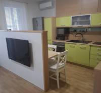 Konyha egy kétszobás lakásban zöld szekrényekkel, televízióval és egy asztallal két székkel.