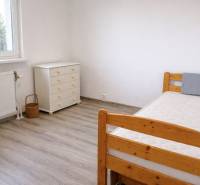 Szoba egy háromszobás lakásban, fa dekorációjú padlóval, ággyal és komóddal.