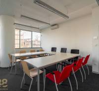 Iroda belső tér hosszú asztallal, színes székekkel és nagy ablakokkal.