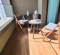 Erkély fa dekorációjú padlóval, ülőhely és díszasztal egy kétszobás lakásban.