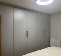 A 3 szobás lakásban fehér tolóajtós szekrények és ágy található.