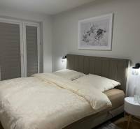 Hálószoba egy háromszobás lakásban világos ággyal és finom fali dekorációval.