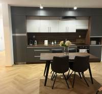 Konyha egy háromszobás lakásban szürke szekrényekkel és fa mintázatú padlóval.