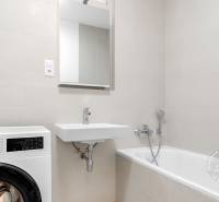 Fürdőszoba egy kétszobás lakásban káddal, mosdóval és mosógéppel fehér árnyalatokban.