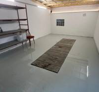 Garázsok polcokkal és világos falakkal, padló járműjavító gödörrel.