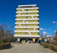 Többszintes lakóépület Komáromban, modern dizájnnal, zölddel és padokkal körülvéve.