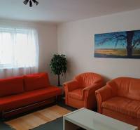 Nappali egy családi házban narancssárga kanapéval, fotelekkel és tájképpel.