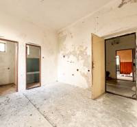 Egy családi házban van egy régi szoba, kopott falakkal és fedetlen helyekkel.