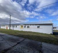 Fehér raktárépület és csarnok Rybkyben, körülvéve fűvel és betonjárdával.